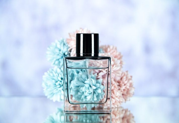Tampilan depan botol parfum dan bunga pada latar belakang buram biru muda (freepik.com)