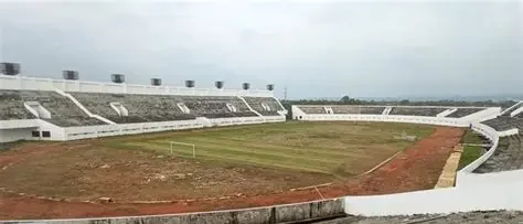 Rumput Stadion Watubelah Menguning, Kang Ohim Soroti Anggaran Perawatan **CIREBON** – Kondisi rumput Stadion Watubelah, Kecamatan Sumber, Kabupaten Cirebon, menjadi sorotan setelah hamparan lapangan utama berubah menjadi kuning kecokelatan dan mengering. Pemandangannya menyerupai sawah yang siap dipanen, berbeda dengan lapangan sepak bola yang seharusnya terlihat hijau dan terawat. Berdasarkan pantauan di lokasi pada Minggu, 18 Oktober 2026, rumput di sebagian besar permukaan lapangan utama terlihat mengering. Kondisi tersebut dilaporkan telah berlangsung lebih dari satu bulan dan memunculkan pertanyaan mengenai pemeliharaan fasilitas olahraga milik publik tersebut. Aktivis Cirebon, Abdulrohim atau yang akrab disapa Kang Ohim, mempertanyakan keseriusan pengelola dalam menjaga kondisi lapangan. Menurutnya, musim kemarau memang dapat memengaruhi pertumbuhan rumput, tetapi perawatan fasilitas seharusnya tetap berjalan. Kritik tersebut tidak hanya menyangkut penampilan lapangan, tetapi juga tanggung jawab pengelola, penggunaan anggaran pemeliharaan, serta pungutan yang dikenakan kepada masyarakat yang berkunjung. ## Kang Ohim Pertanyakan Pemeliharaan Stadion Watubelah Kang Ohim menilai kondisi rumput yang mengering perlu menjadi perhatian serius. Ia mempertanyakan pola pemeliharaan yang dilakukan hingga lapangan utama Stadion Watubelah mengalami perubahan warna secara luas. Menurutnya, fasilitas olahraga yang memiliki pengelola seharusnya mendapatkan perawatan rutin, termasuk ketika menghadapi cuaca kering. Pemeliharaan tersebut diperlukan agar kondisi rumput tidak semakin memburuk dan lapangan tetap dapat dimanfaatkan sesuai fungsinya. Ia juga mempertanyakan klaim mengenai perawatan rumput melalui penyiraman dan pemupukan. Kondisi lapangan yang terlihat saat ini, menurutnya, menimbulkan keraguan terhadap efektivitas pemeliharaan tersebut. Kang Ohim menilai persoalan ini tidak semestinya hanya dijelaskan melalui faktor cuaca. Pengelola perlu memberikan keterangan mengenai langkah perawatan yang telah dilakukan dan upaya yang disiapkan untuk menangani kondisi rumput. ## Anggaran Perawatan Ikut Menjadi Sorotan Selain kondisi lapangan, penggunaan anggaran pemeliharaan turut dipertanyakan. Kang Ohim menyoroti peran Dinas Pemuda dan Olahraga (Dispora) Kabupaten Cirebon dalam kaitannya dengan anggaran perawatan Stadion Watubelah. Ia mempertanyakan sejauh mana anggaran tersebut digunakan dan bagaimana hasil pemeliharaannya dapat dilihat secara nyata. Sorotan ini penting karena perawatan lapangan sepak bola membutuhkan penanganan yang berkelanjutan. Penyiraman, pemupukan, pemotongan rumput, serta pemeriksaan kondisi tanah merupakan beberapa aspek yang perlu diperhatikan agar kualitas lapangan tetap terjaga. Namun, kondisi rumput yang mengering belum cukup untuk membuktikan adanya penyimpangan dalam penggunaan anggaran. Diperlukan penjelasan mengenai alokasi dana, kegiatan pemeliharaan yang telah dilaksanakan, serta evaluasi hasil perawatan untuk mengetahui persoalan secara menyeluruh. Karena itu, transparansi dari pihak terkait dibutuhkan agar masyarakat memperoleh informasi yang jelas mengenai pengelolaan fasilitas olahraga tersebut. ## Pungutan Pengunjung Juga Dipertanyakan Persoalan lain yang disoroti Kang Ohim adalah pungutan terhadap pengunjung Stadion Watubelah. Ia menyebut masyarakat harus membayar karcis parkir dan kembali dikenai tarif ketika memasuki area stadion. Menurutnya, mekanisme pungutan dan penggunaan pendapatan dari aktivitas kawasan stadion perlu dijelaskan secara terbuka. Ia mempertanyakan apakah penerimaan tersebut turut mendukung biaya operasional dan pemeliharaan fasilitas. Kondisi ini memunculkan pertanyaan mengenai hubungan antara pengelolaan kawasan stadion dan kualitas fasilitas yang dapat dinikmati masyarakat. Kejelasan mengenai dasar penarikan tarif, pihak yang bertanggung jawab, serta peruntukan penerimaan menjadi penting agar pengelolaan fasilitas publik dapat dipertanggungjawabkan. ## Warga Kecewa Melihat Kondisi Rumput Kondisi rumput yang mengering juga menimbulkan kekecewaan bagi warga yang datang untuk berolahraga. Naim, salah seorang warga yang berkunjung ke Stadion Watubelah untuk berjoging, mengaku terkejut melihat perubahan kondisi lapangan. Ia menyebut rumput stadion beberapa bulan sebelumnya masih terlihat hijau. Menurutnya, kondisi tersebut sangat disayangkan karena Stadion Watubelah memiliki potensi menjadi ruang olahraga yang nyaman bagi masyarakat. Keluhan warga ini memperlihatkan bahwa pemeliharaan stadion tidak hanya berkaitan dengan kebutuhan atlet atau penyelenggaraan pertandingan. Kondisi fasilitas juga memengaruhi pengalaman masyarakat yang memanfaatkan kawasan tersebut untuk beraktivitas fisik. ## Perlu Evaluasi dan Penjelasan Pengelola Musim kemarau dapat meningkatkan risiko kekeringan pada rumput lapangan terbuka. Berkurangnya ketersediaan air dan meningkatnya penguapan dapat membuat rumput berubah warna, terutama jika kebutuhan air tidak terpenuhi. Meski demikian, penyebab pasti kondisi rumput Stadion Watubelah tetap perlu dipastikan melalui pemeriksaan lapangan. Evaluasi diperlukan untuk mengetahui apakah kekeringan dipengaruhi oleh cuaca, kondisi tanah, sistem penyiraman, atau faktor pemeliharaan lainnya. Hingga berita ini disusun, sumber pemberitaan yang tersedia belum memuat penjelasan resmi pengelola mengenai penyebab rumput mengering, kegiatan perawatan yang telah dilakukan, maupun rencana pemulihan lapangan. Kondisi ini menjadi pengingat bahwa pengelolaan fasilitas olahraga publik perlu disertai pemeliharaan berkelanjutan dan transparansi. Masyarakat tentu berharap Stadion Watubelah tetap menjadi tempat olahraga yang layak, nyaman, dan terawat. Penjelasan dari pihak pengelola dan instansi terkait kini diperlukan untuk menjawab pertanyaan mengenai kondisi rumput, penggunaan anggaran perawatan, serta langkah konkret yang akan dilakukan agar lapangan kembali berfungsi secara optimal